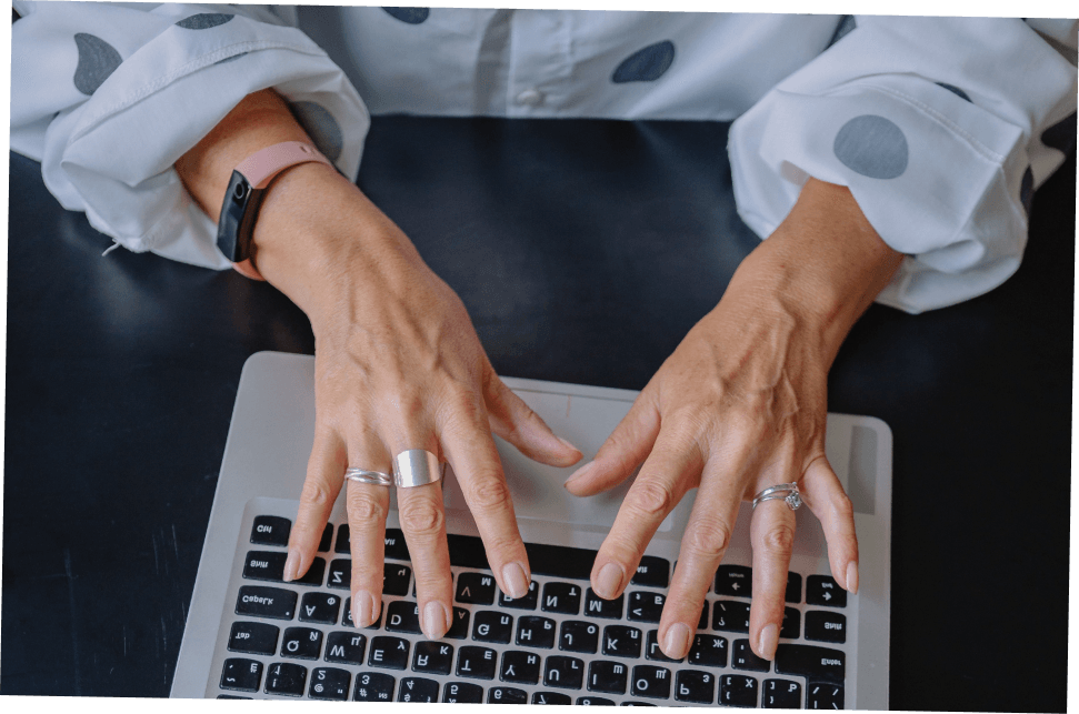 Hands typing on a laptop, wearing rings and a pink watch