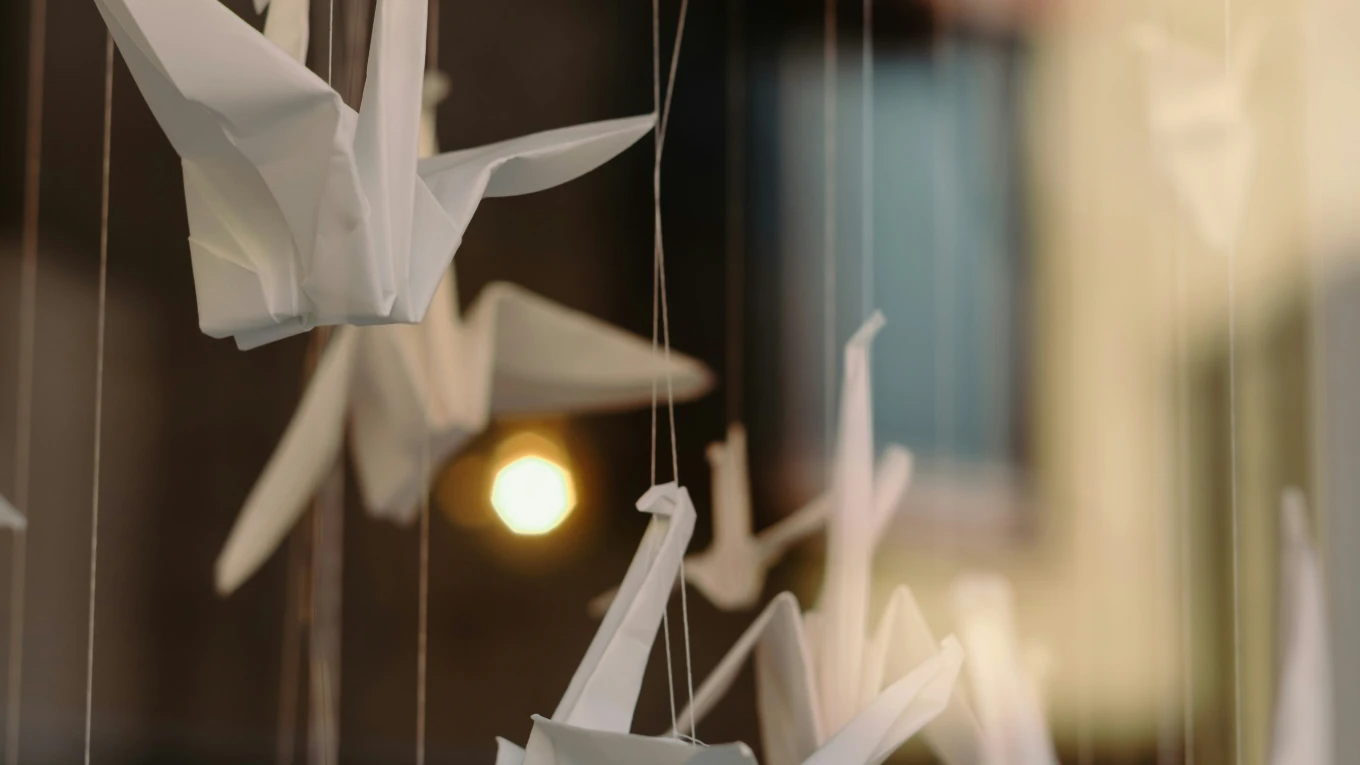 Paper cranes hanging on threads in front of a warm light