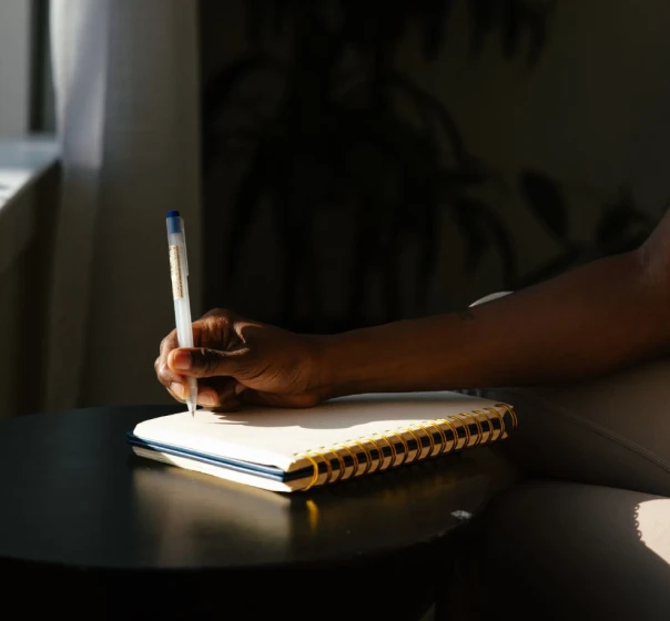 A hand writing in a spiral notebook on a dark table