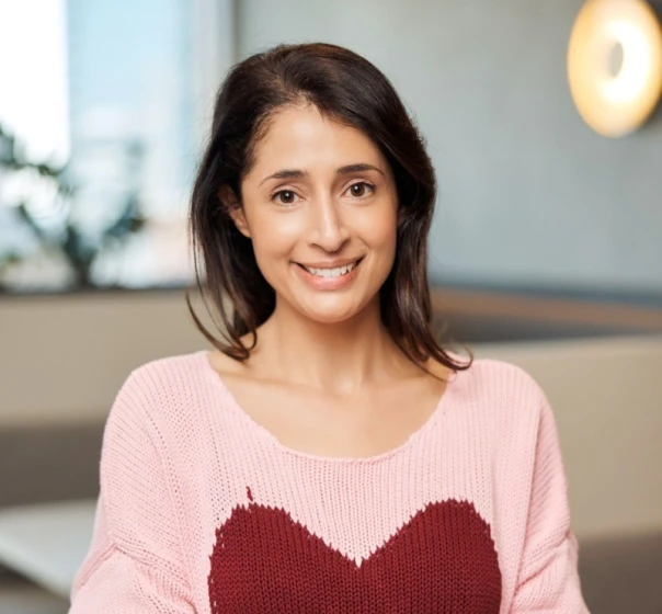 A smiling woman in a pink jumper with a red heart