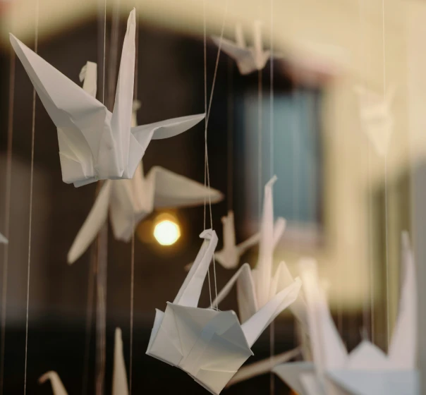 Paper cranes hanging in front of a warm light